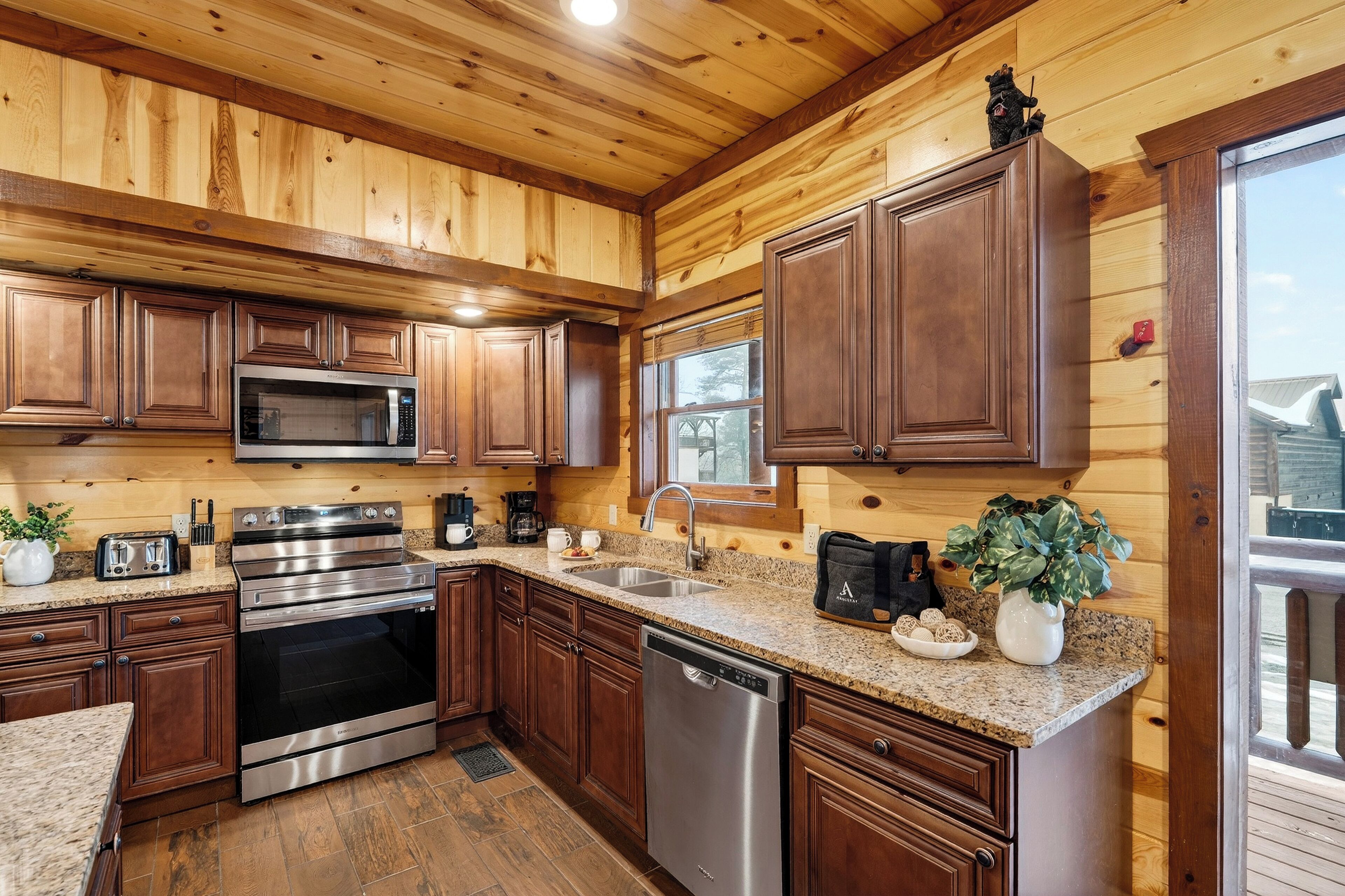 A modern kitchen with wooden paneling, stainless steel appliances, granite countertops, and a large window.