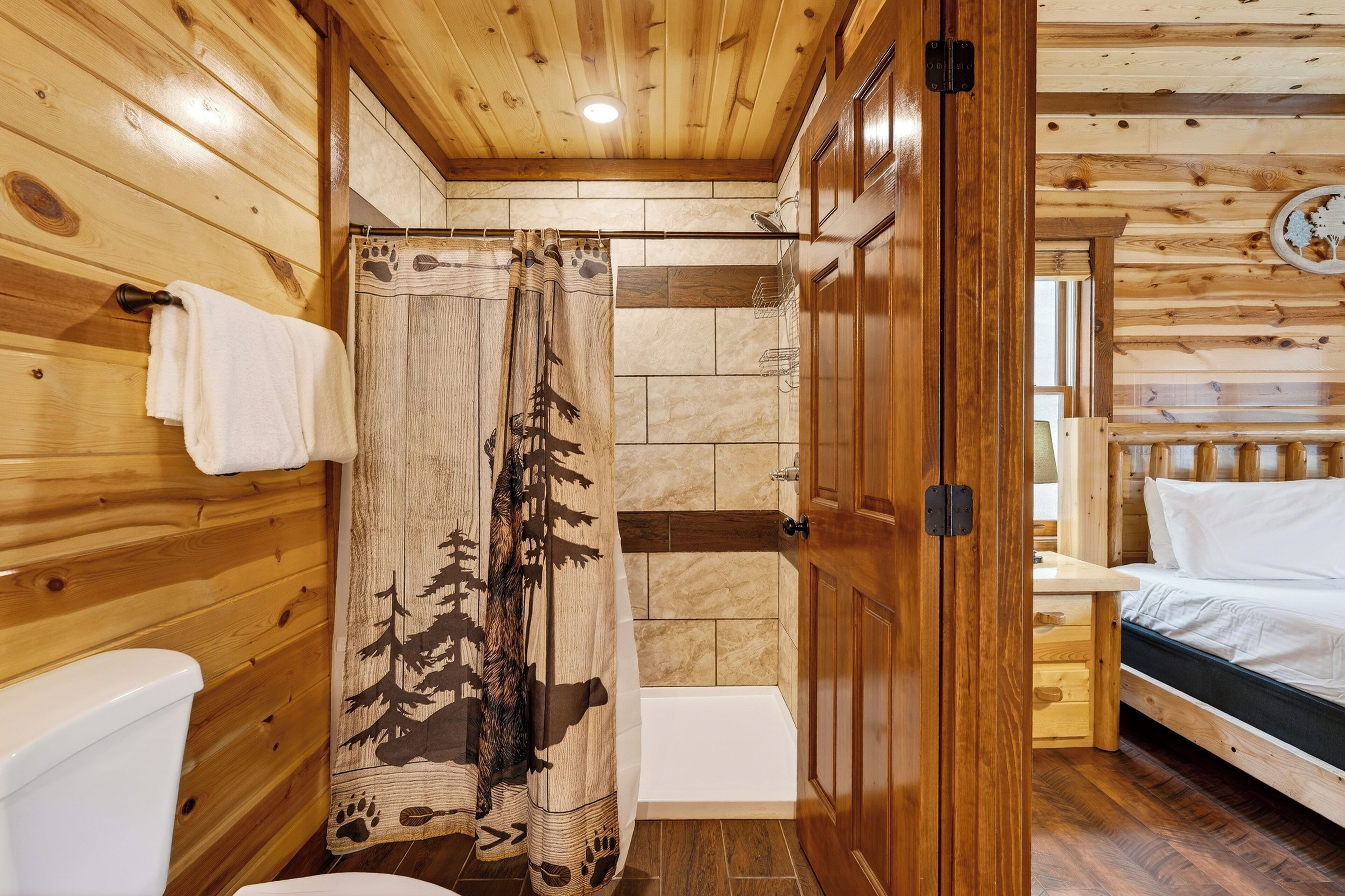 A wooden cabin bathroom with a shower curtain featuring a forest design, a toilet, and a bed with a wooden headboard.