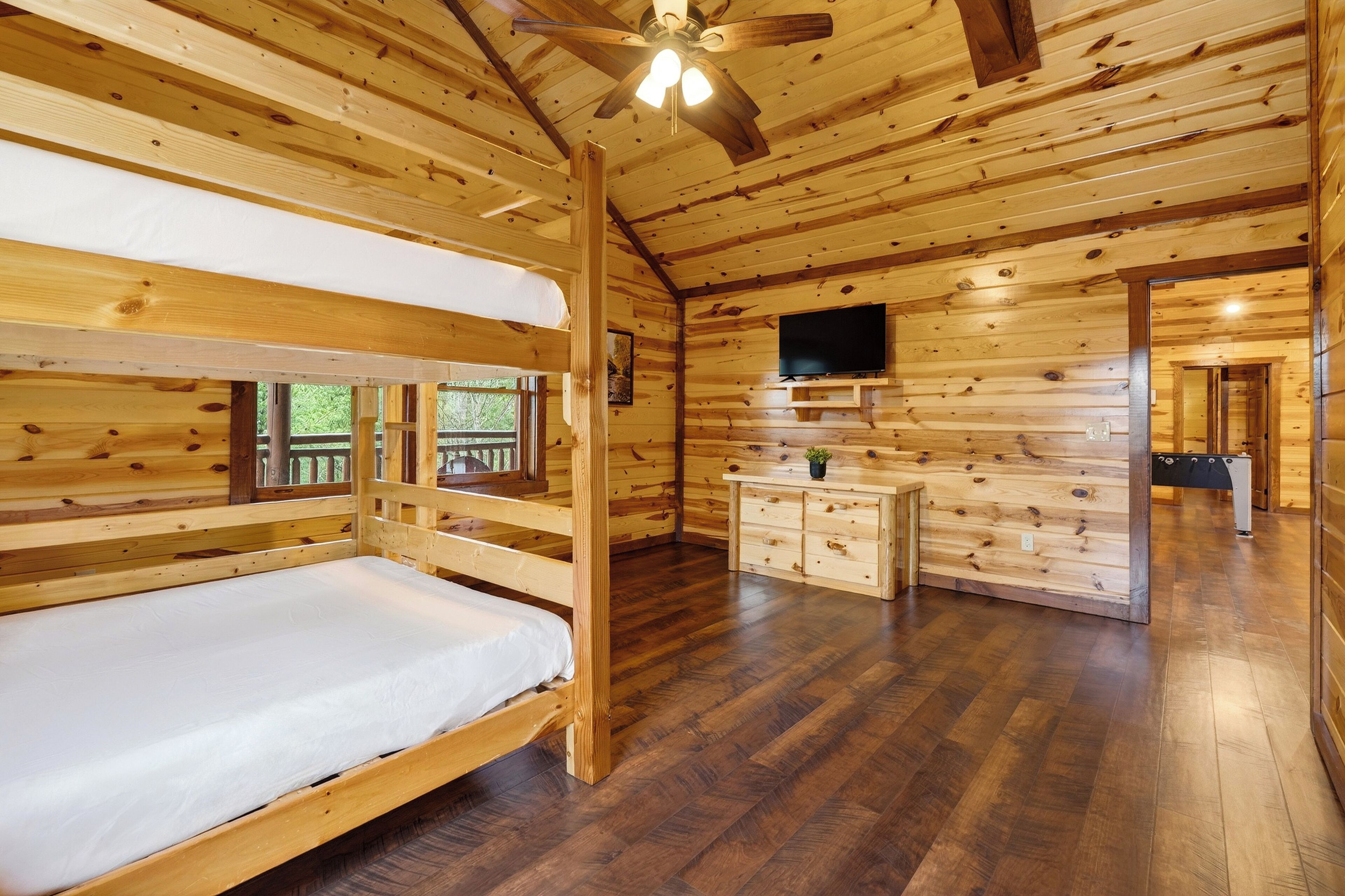 A wooden cabin with bunk beds, a TV, a dresser, and a ceiling fan.