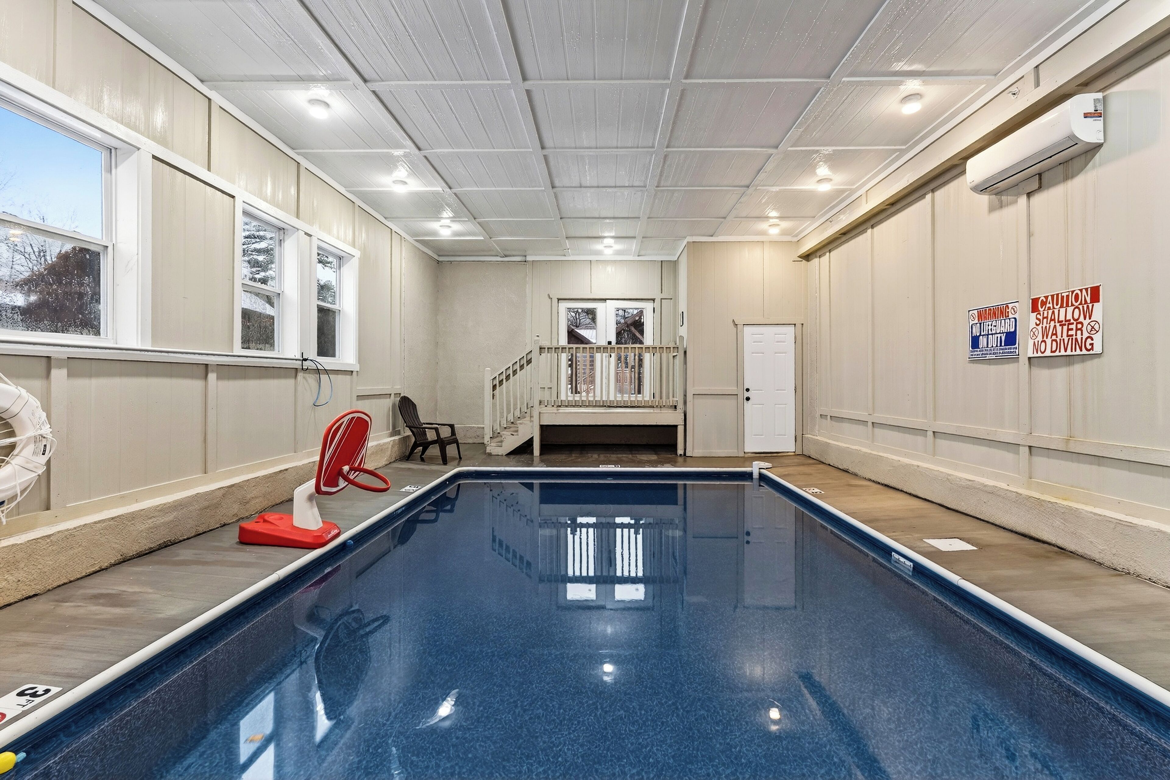 An indoor swimming pool with a clear view of the pool area, a staircase, and a door leading to another room.