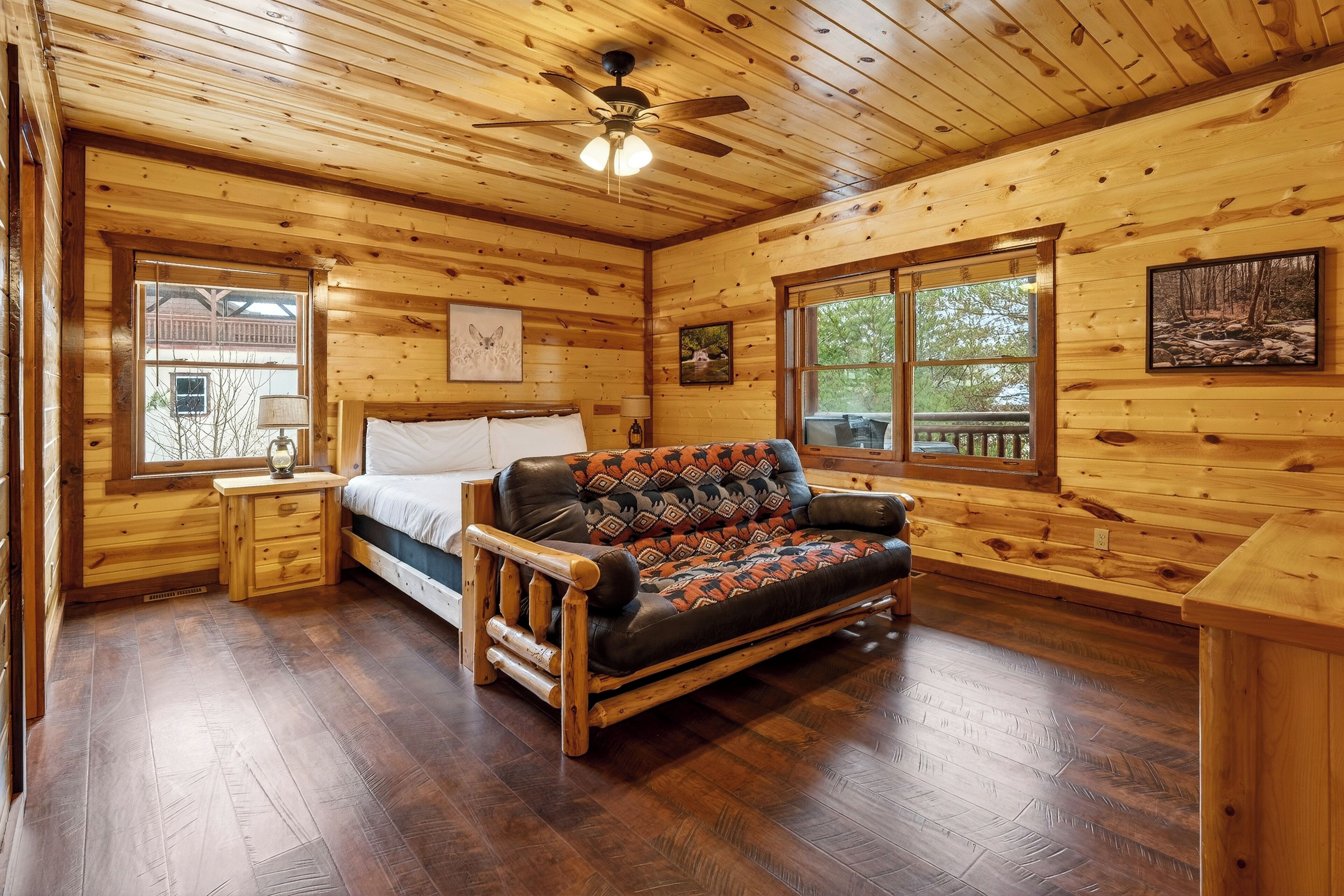 A log cabin bedroom with a bed, a sofa, wooden floors, and large windows.