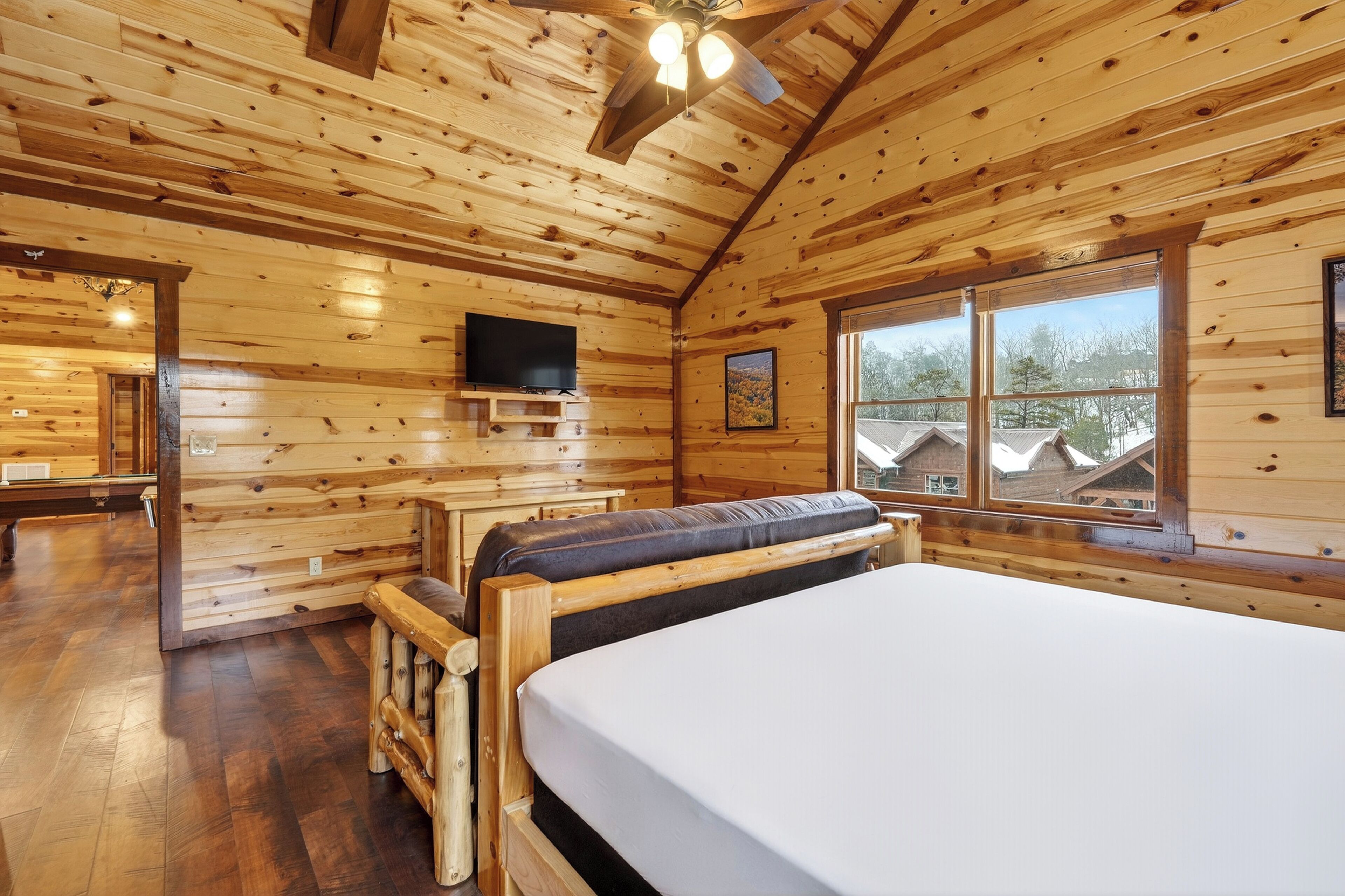 A wooden cabin room with a bed, a TV, and large windows.