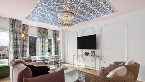 A modern living room with a large window, a flat-screen TV, a white coffee table, a pink sofa, and a wicker chair. - Hottub + Speakeasy Lounge + Premium Karaoke + Rooftop + Near Downtown Nashville (Nashville)