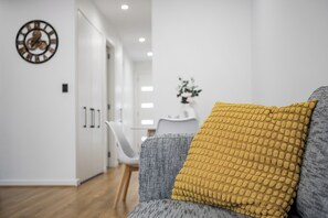 A modern living room with a sofa, a yellow textured pillow, and a wall clock. - Relax by the Beach, Close to Everything - Minutes from City & Airport! (Flinders Park)