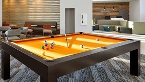 Une table de billard dans un salon moderne, doté d’un espace détente avec des sièges et un bar.