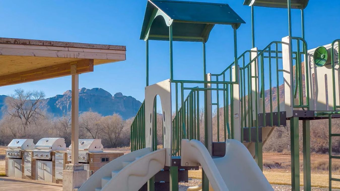 A playground with a slide and climbing structures, set against a backdrop of mountains.