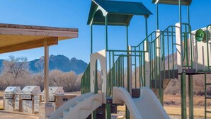 Un terrain de jeux équipé d’un toboggan et de structures d’escalade, avec une chaîne de montagnes en toile de fond.