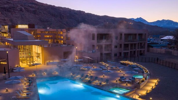 Un complexe hôtelier doté d’une piscine, de chaises longues et offrant une vue sur un paysage montagneux.