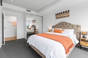 A bedroom with a large bed, a nightstand, a mirror, and a wall-mounted artwork.