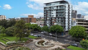 A modern multi-story building with balconies, surrounded by greenery and a landscaped area with a circular garden feature. - Adelaide Parkside Escape | 2BR + Gym + Parking (Adelaide)