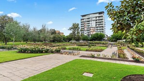 A landscaped garden with pathways, a building in the background, and a clear sky. - Adelaide Parkside Escape | 2BR + Gym + Parking (Adelaide)