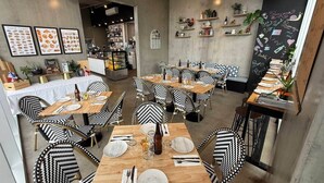 A restaurant with multiple tables and chairs, a chalkboard menu, and various kitchen items in the background. - Adelaide Parkside Escape | 2BR + Gym + Parking (Adelaide)