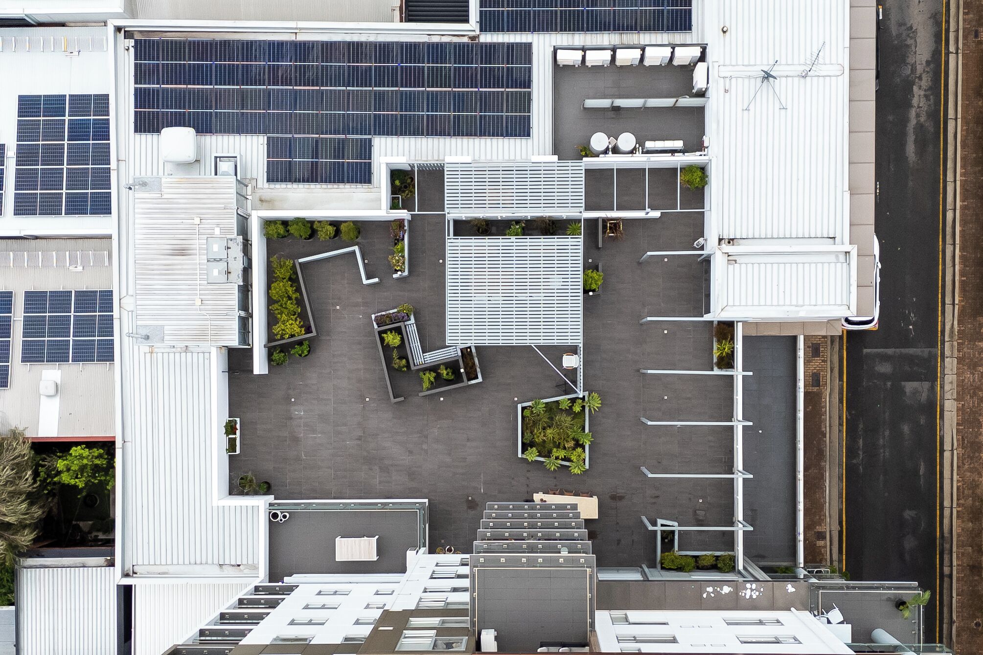 An aerial view of a building with multiple floors, solar panels, and a parking area with designated spaces.
