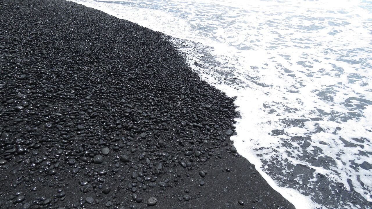 Una playa con piedras negras y olas.
