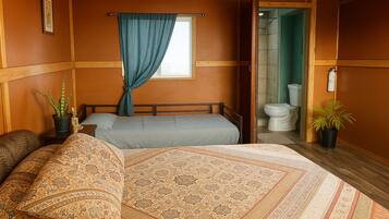 A room with two beds, a window with blue curtains, a toilet, and potted plants.