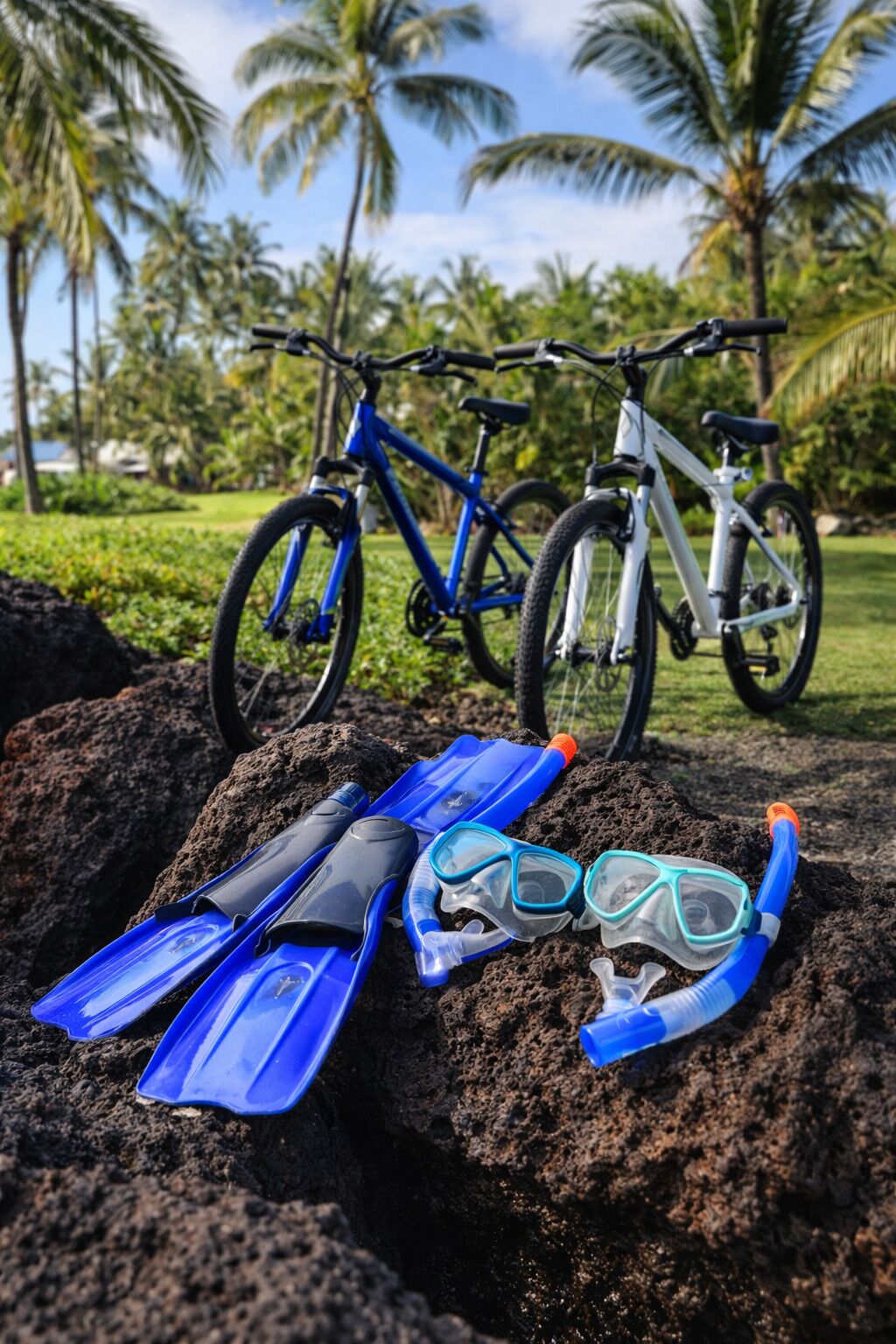 A pair of blue snorkeling fins and a snorkel on a rock with bicycles in the background.