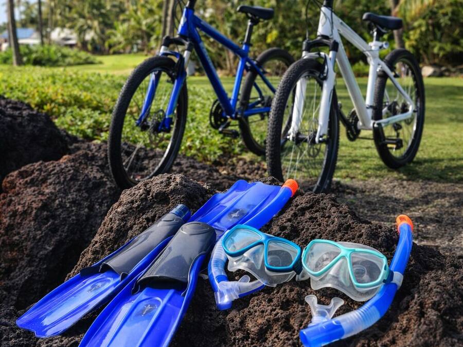 A pair of blue snorkeling fins and a snorkel on a rock with bicycles in the background.