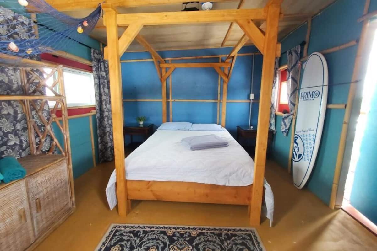 A room with a bed, a wooden headboard, a surfboard, and a patterned rug.