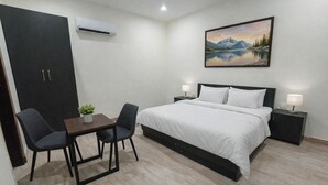 A modern bedroom with a bed, bedside tables, a desk with chairs, and a painting on the wall. - Bodhi Residency (Greater Noida)