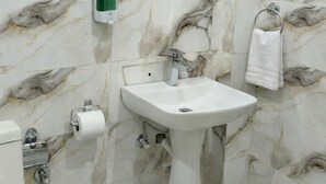 A bathroom with marble-patterned walls, a sink, a mirror, a towel rack, and a toilet. - Bodhi Residency (Greater Noida)