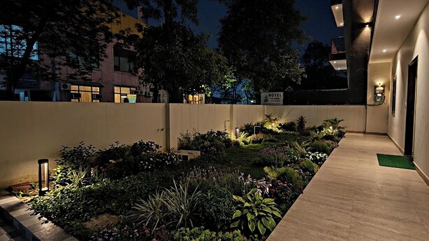 A hotel exterior at night with a well-lit garden, a pathway, and a sign indicating the hotel's location. - Bodhi Residency (Greater Noida)