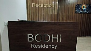 A reception desk with 'Reception' and 'BODHI Residency' signage, a wooden wall, and a framed picture. - Bodhi Residency (Greater Noida)
