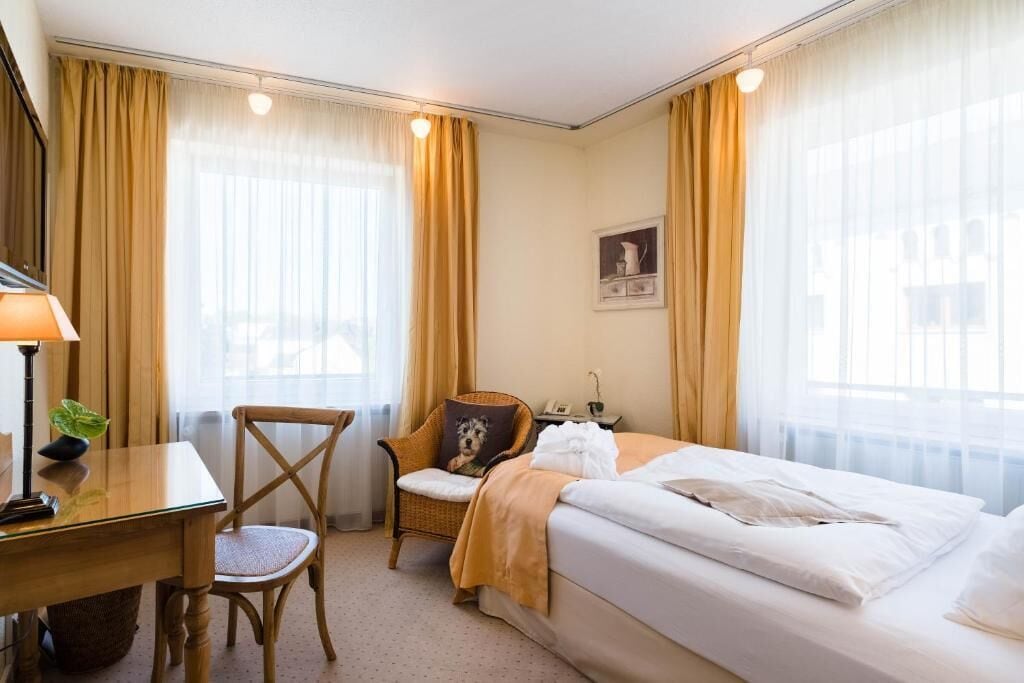 Une chambre d’hôtel avec un lit, un bureau, une chaise et une fenêtre avec des rideaux.