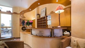 A reception area with a curved counter, wicker furniture, a lamp, and a vase with flowers. - Hotel zur Mühle (Paderborn)