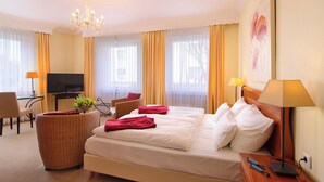 A hotel room with a large bed, a television, a desk with a computer, a wicker chair, and a lamp. - Hotel zur Mühle (Paderborn)