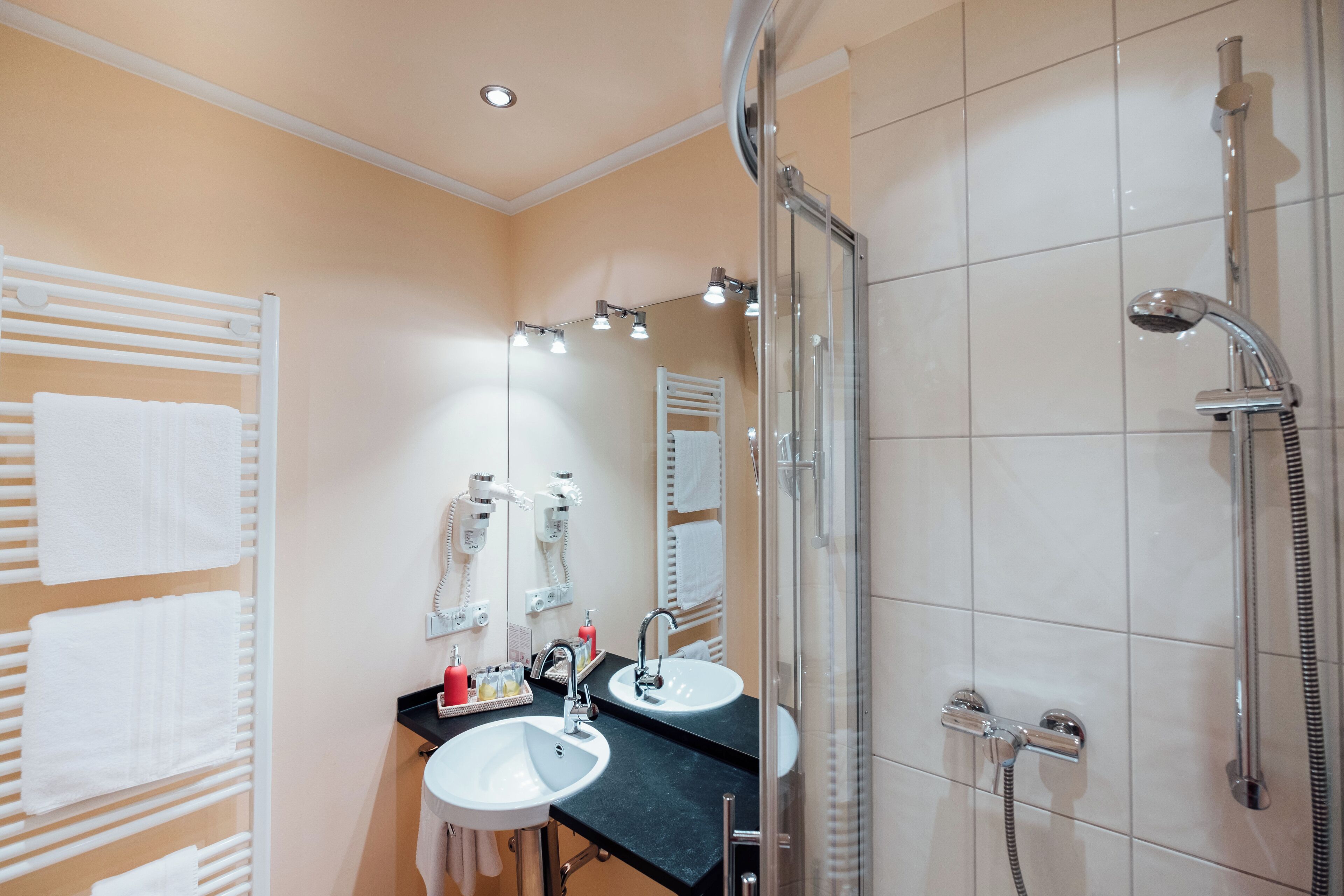 A bathroom with two sinks, a glass shower enclosure, and a towel rack with multiple towels.