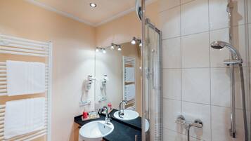 A bathroom with two sinks, a glass shower enclosure, and a towel rack with multiple towels.