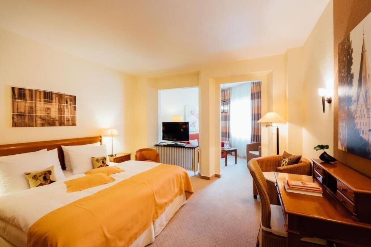 A hotel room with a large bed, a desk, a chair, and a television.