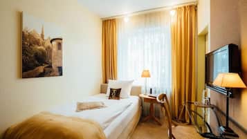 Una habitación de hotel con cama, escritorio, silla, lámpara, televisión y un cuadro en la pared.