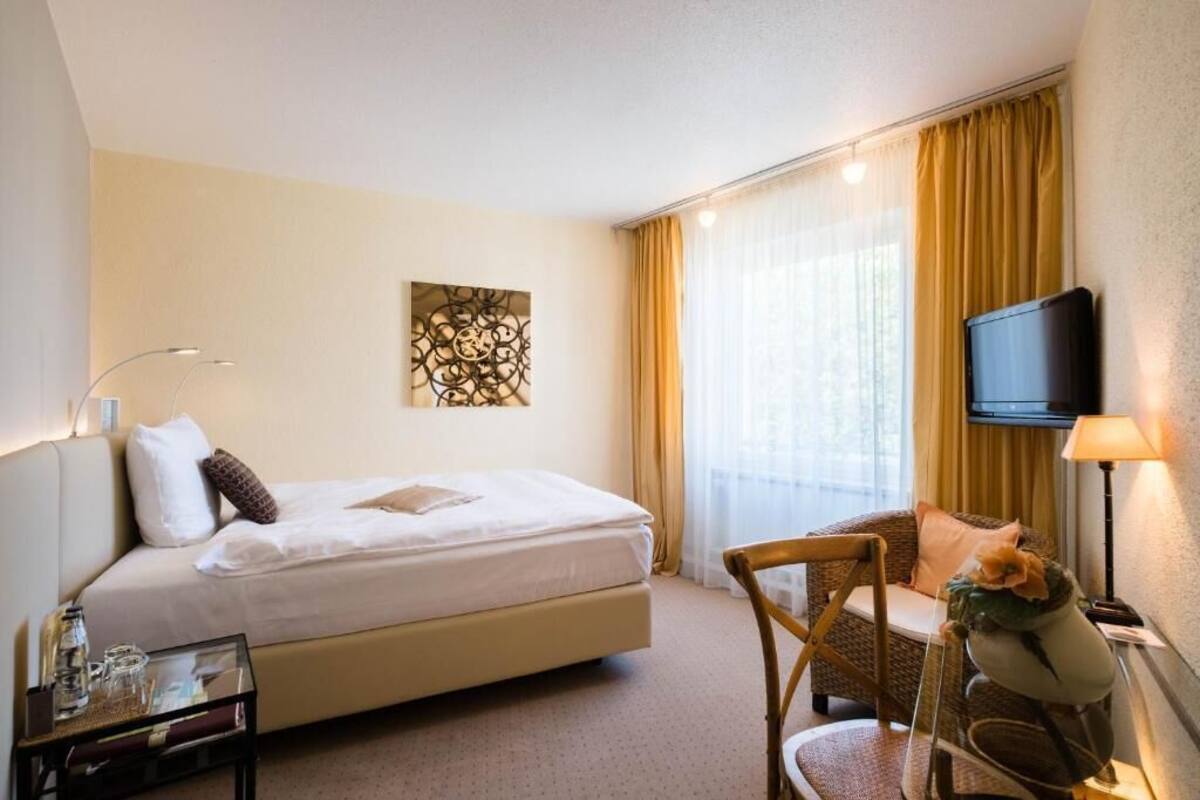 A hotel room with a bed, a chair, a TV, and a window with curtains.