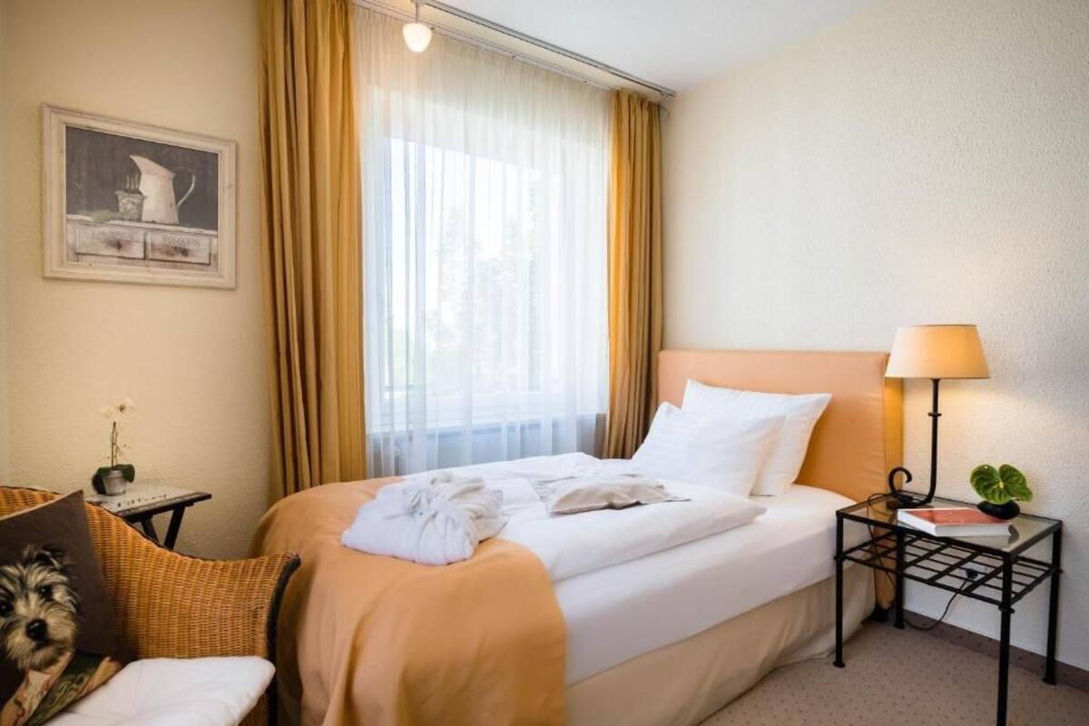 A hotel room with a bed, a nightstand with a lamp, a chair, and a painting on the wall.