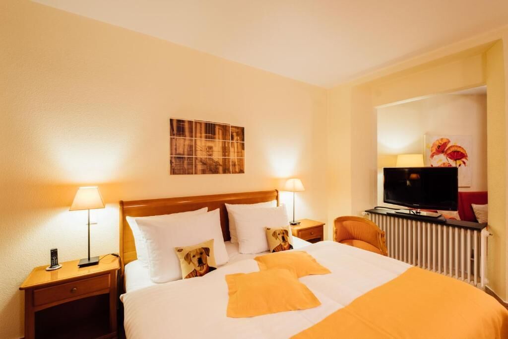 Een hotelkamer met een bed, twee nachtkastjes met lampen, een televisie en een schilderij aan de muur.