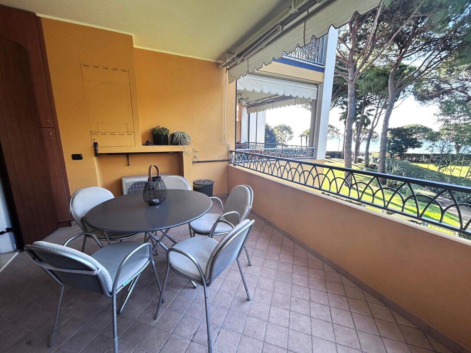 Een balkon met een ronde tafel en stoelen, een kleine potplant en uitzicht op een park.