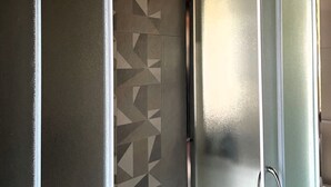 Un baño con pared de diseño geométrico, una puerta de vidrio esmerilado y un tirador metálico.