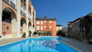 A swimming pool with a clear blue water surface, surrounded by a building with arched balconies and a stone wall. - Mansarda del Gallo_Penthouse with Lake View and Swimming Pool (Salò)