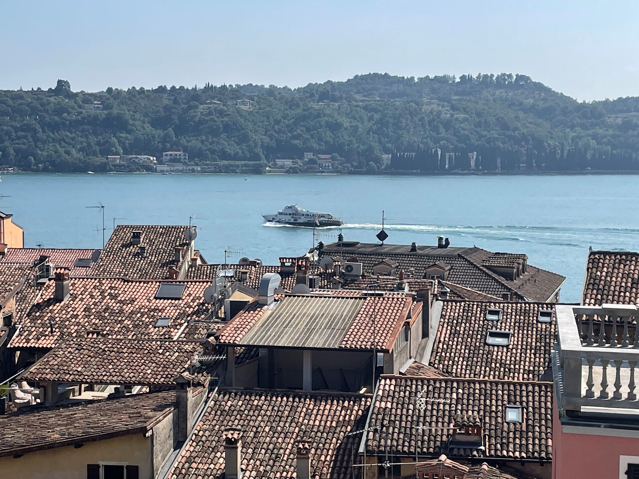 Un paysage urbain côtier avec des toits recouverts de tuiles en terre cuite, une étendue d’eau et un bateau au loin.