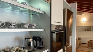 A modern kitchen with white cabinetry, a stainless steel refrigerator, and a coffee station with a Keurig machine and coffee cups. - Mansarda del Gallo_Penthouse with Lake View and Swimming Pool (Salò)