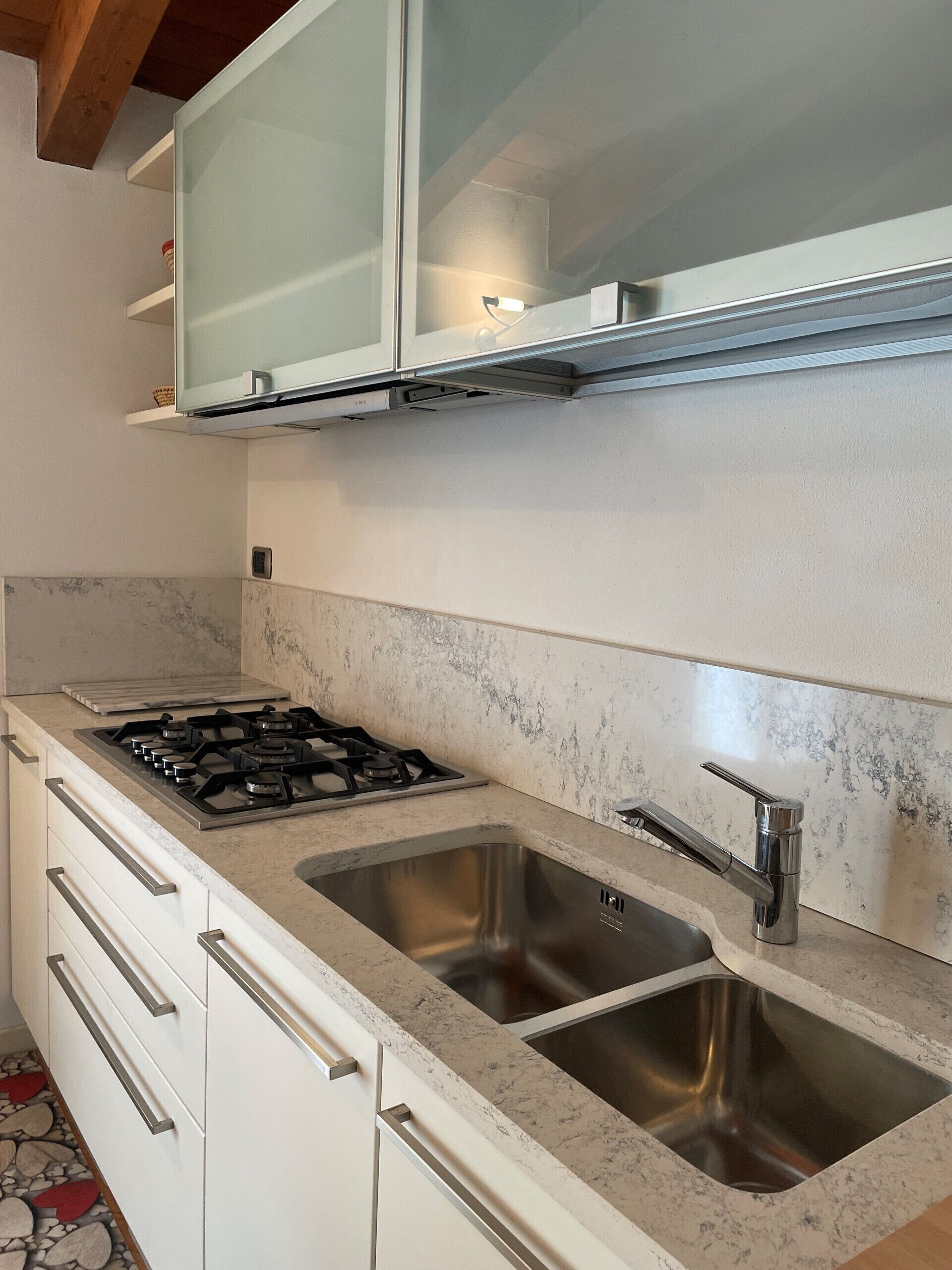 Een keuken met een gasfornuis, een roestvrijstalen spoelbak en witte kasten.
