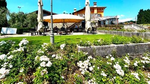 Un área de estar al aire libre con mesas y sillas, rodeada de un jardín con flores blancas.