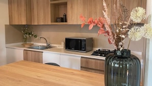 Una cocina moderna con armarios de madera, microondas, pileta y un florero con flores secas sobre la encimera.