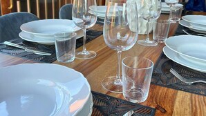 Una mesa de comedor con platos blancos, vasos transparentes y cubiertos, con un florero decorativo de plantas verdes en el centro.