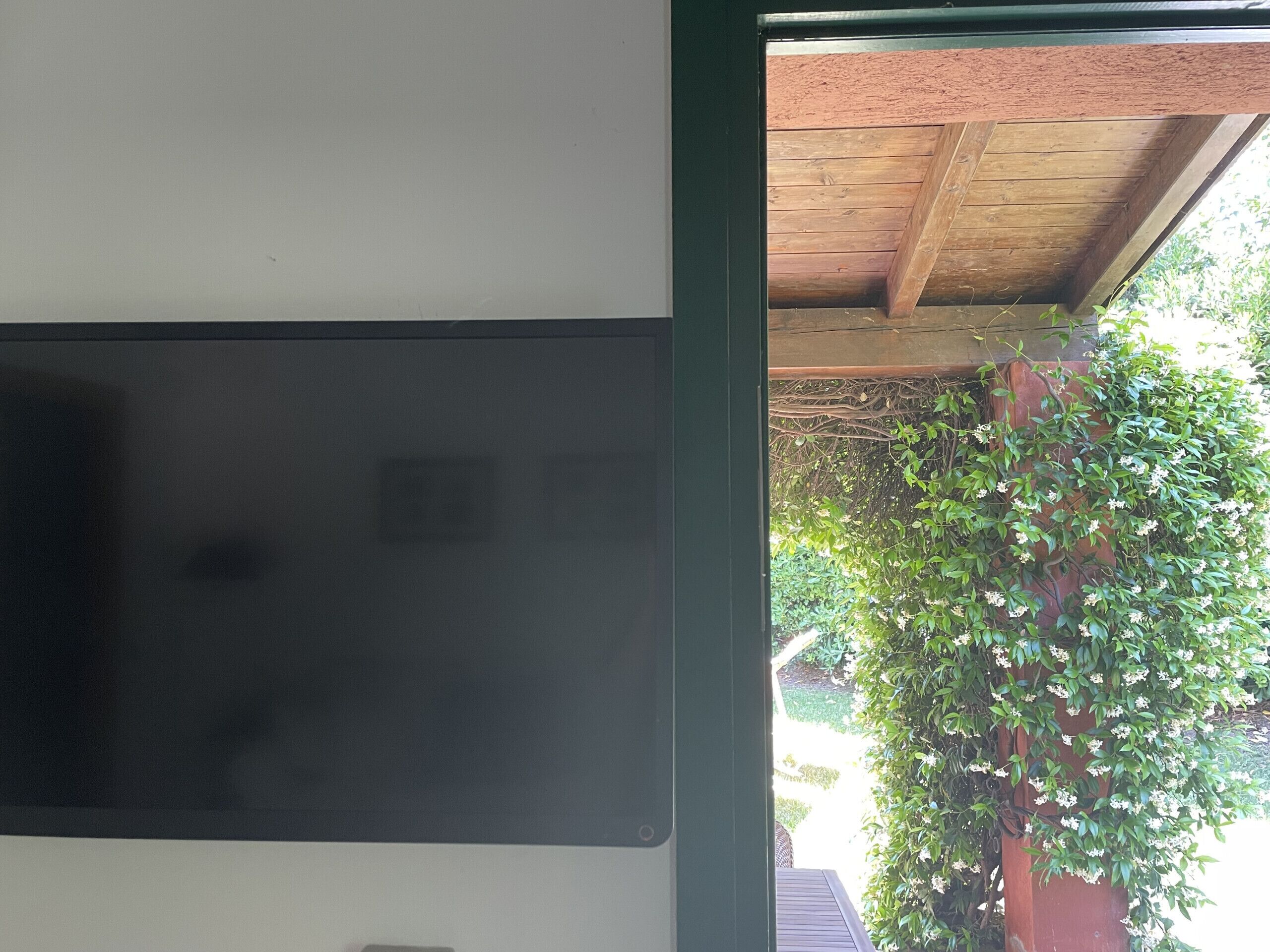 Une pièce dotée d’un grand écran noir, d’un plafond en bois et offrant une vue sur un arbre verdoyant à l’extérieur.