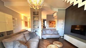 A modern living room with a sofa, ottomans, a TV, and a unique chandelier. - Casa Magenta_Private Garden & Swimming Pool in the Village (Moniga del Garda)