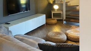 A modern living room with a staircase, a flat-screen TV, a white console, and woven poufs. - Casa Magenta_Private Garden & Swimming Pool in the Village (Moniga del Garda)