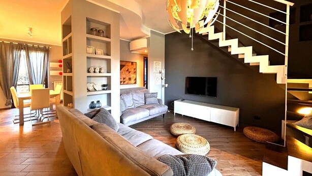 A modern living room with a sofa, TV, and a staircase. - Casa Magenta_Private Garden & Swimming Pool in the Village (Moniga del Garda)