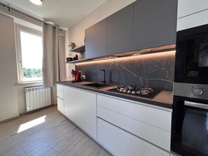A modern kitchen with a gas stove, built-in oven, and a window with curtains. - The cottage at Borgo Alba_Charm in a historic courtyard (Polpenazze del Garda)
